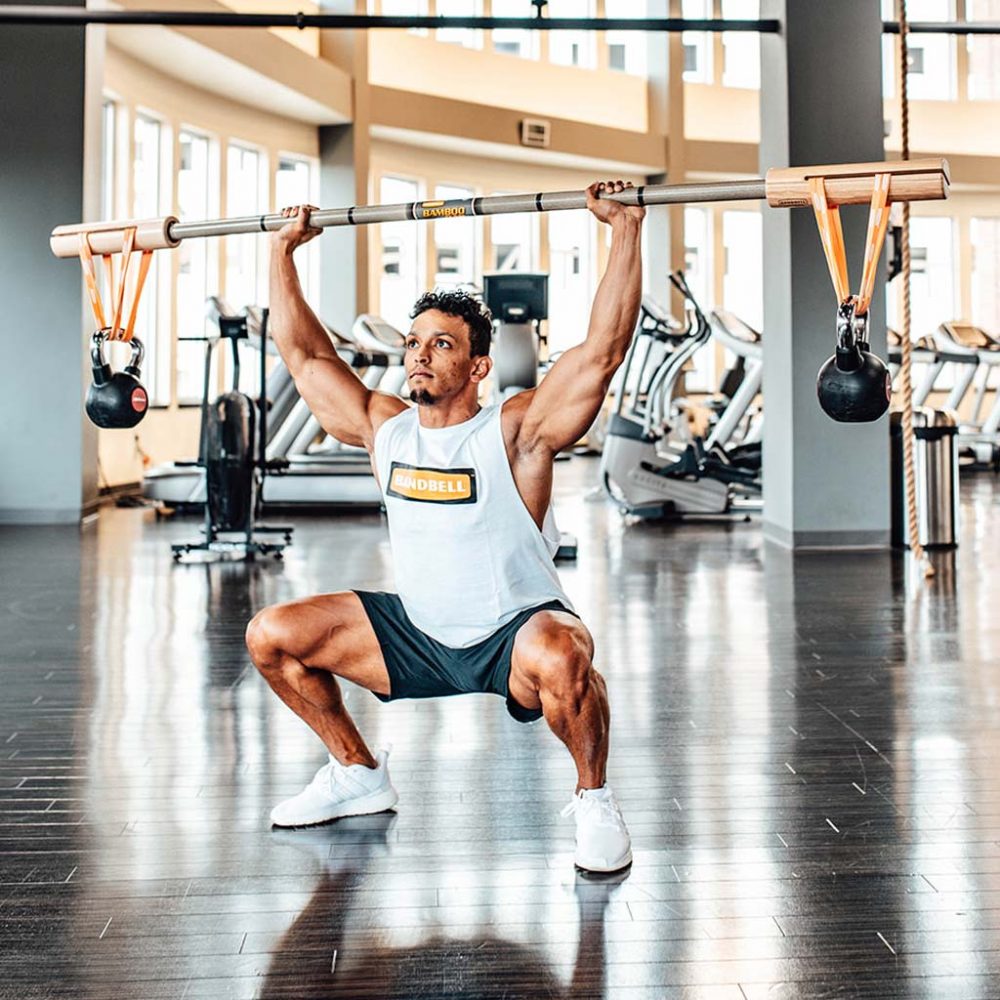 man squatting with bamboo bar overhead